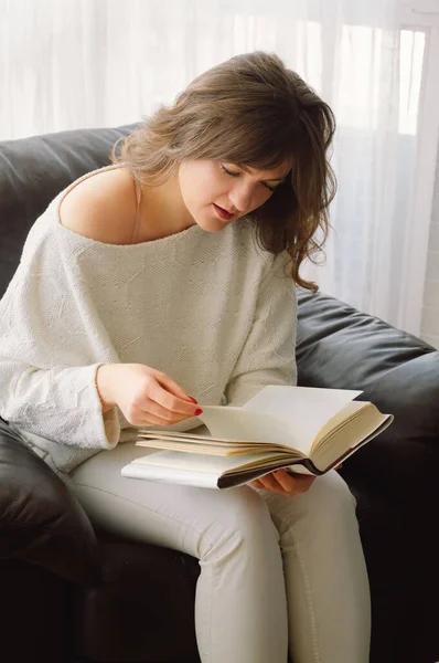Beleza jovem está lendo um livro em casa. Menina pensativa lendo livro importante — Fotografia de Stock
