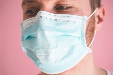 Pembe arka planda viral maskeli bir adam. Koronavirüsü önlemek için yüz koruması takıyor.