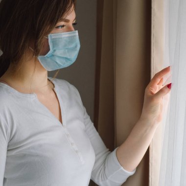 Coronavirus covid-19. Koruyucu maskeli bir kadın pencerenin yanında duruyor.