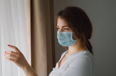 Coronavirus covid-19. Koruyucu maskeli bir kadın pencerenin yanında duruyor.