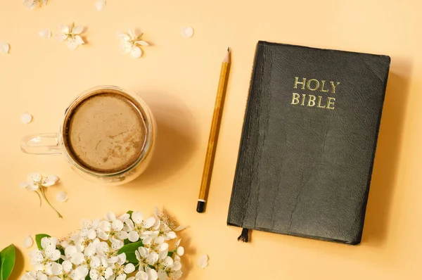 The Bible and cup coffee with spring flowers on a color background. Concept for faith, spirituality and religion