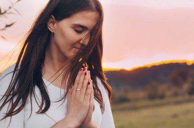 Dua eden ve gün batımını seyreden bekar bir kadının portresi. İnanç için dua kavramına sarılmış eller.