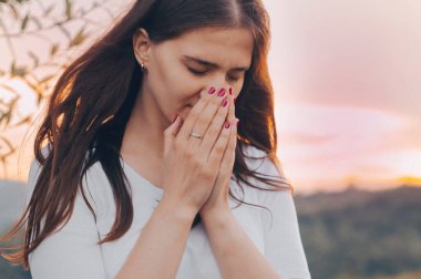 Dua eden ve gün batımını seyreden bekar bir kadının portresi. İnanç için dua kavramına sarılmış eller.
