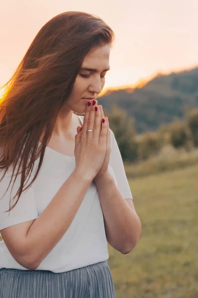 รูปภาพของผู้หญิงคนเดียวอธิษฐานและมองลงไปที่พระอาทิตย์ตกดิน มือพับในแนวคิดการสวดมนต์เพื่อความเชื่อ — ภาพถ่ายสต็อก