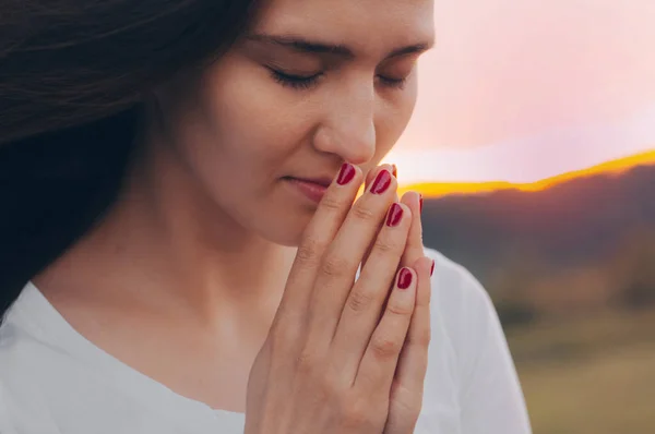 Potret seorang wanita yang sedang berdoa dan melihat ke bawah saat matahari terbenam. Tangan dilipat dalam konsep doa untuk iman — Stok Foto