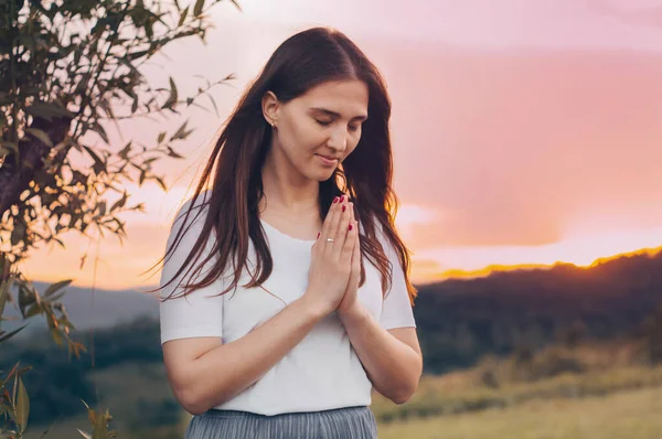 Dua eden ve gün batımını seyreden bekar bir kadının portresi. İnanç için dua kavramına sarılmış eller.