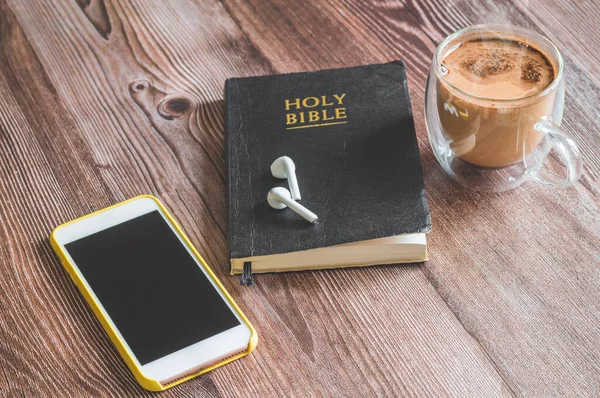 La Sacra Bibbia con le cuffie, un telefono e una tazza di caffè caldo. Leggere la Bibbia . — Foto Stock