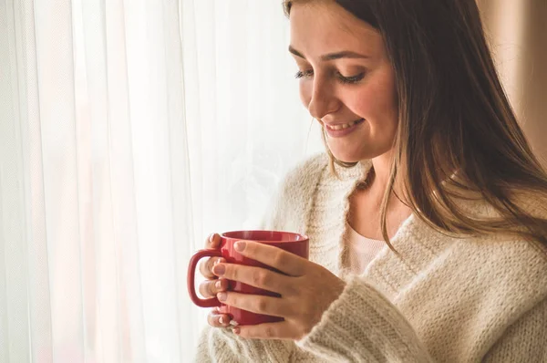 Mujer con una taza de bebida caliente junto a la ventana. Buenos días con el té. Otoño Invierno . — Foto de Stock