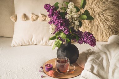 Still life details in home interior of living room. Lilac flowers with hot cup tea.  clipart