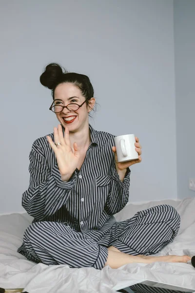 Wanita dalam piyama memegang cangkir kopi di tempat tidurnya — Stok Foto