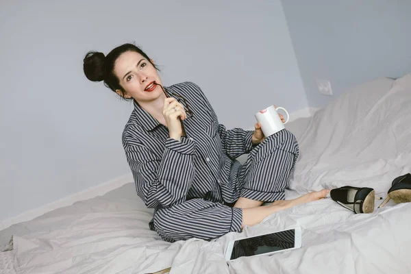Woman in pajamas holding coffee cup on her bed — Stock Photo, Image