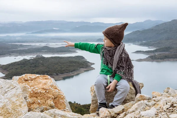 Schattige jongen in een grappige hoed zittend op een berg. Concept van de vrijheid — Stockfoto