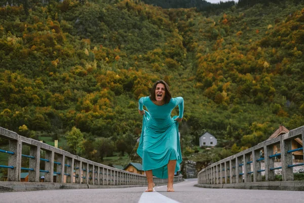 Mujer joven en un elegante vestido de color turquesa grita en el puente — Foto de Stock