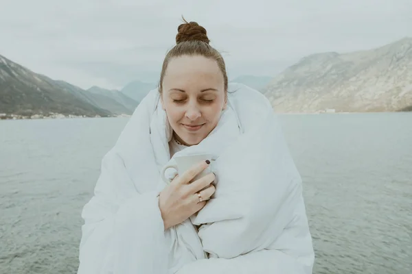 Mujer escondiendo manta blanca con taza de café de pie en un muelle —  Fotos de Stock