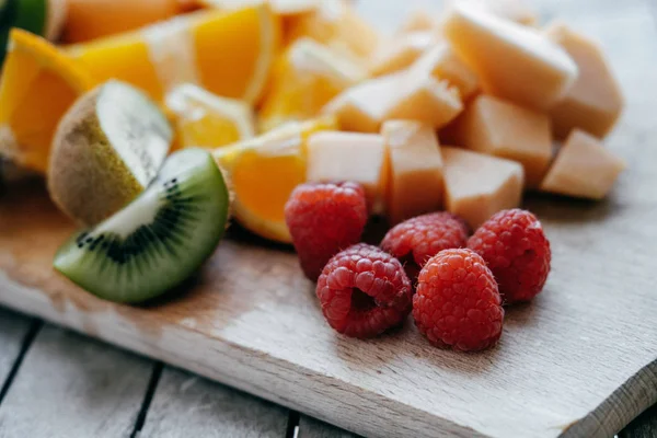 Fruta fresca en rodajas: frambuesa, kiwi, melón, naranjas sobre una madera —  Fotos de Stock