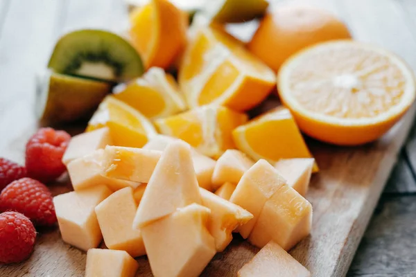 Свіжі нарізані фрукти: малина, ківі, диня, апельсини на дерев'яній — стокове фото