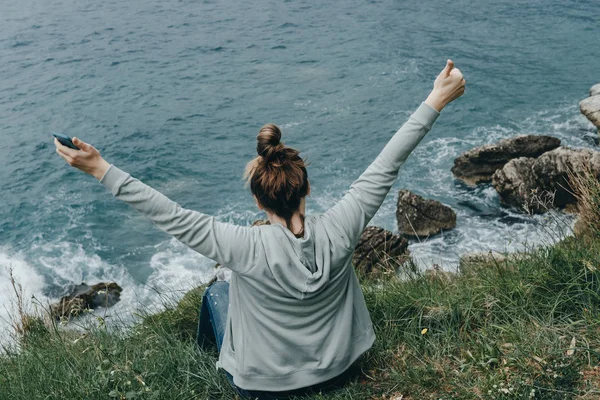 Achteraanzicht van de vrouw aan de orde gesteld haar handen omhoog zittend op de berg — Stockfoto