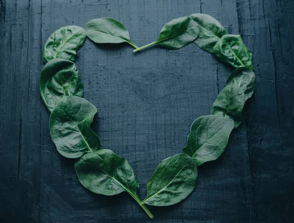 Leaves of fresh spinach in the form of heart on a black board — Stock Photo, Image