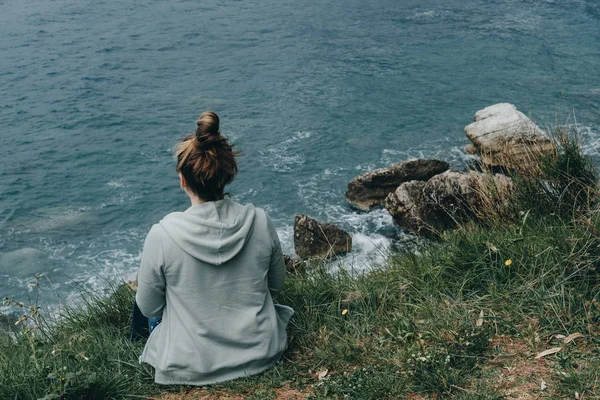 Jonge vrouw in een groen jasje kijkt naar de zee vanaf de berg — Stockfoto