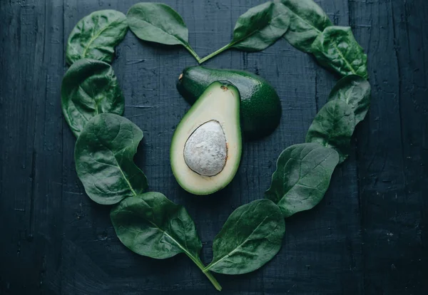 Avocado and spinach in the form of heart on black board backgrou — Stock Photo, Image