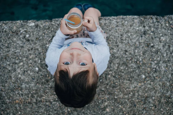 Niño bebiendo jugo en el muelle junto al mar — Foto de Stock
