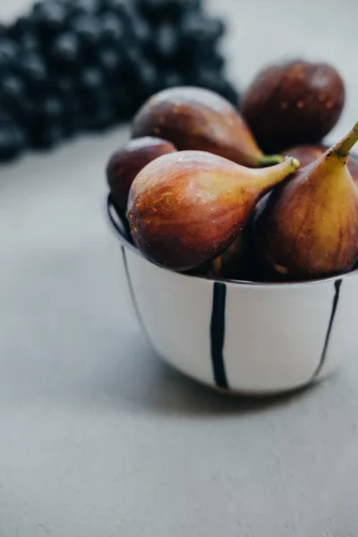 Higos en un tazón y uvas oscuras sobre un fondo gris. Otoño harv —  Fotos de Stock