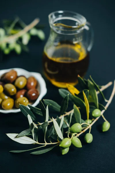 Свежие оливки, масло и зеленая ветвь на черном фоне — стоковое фото