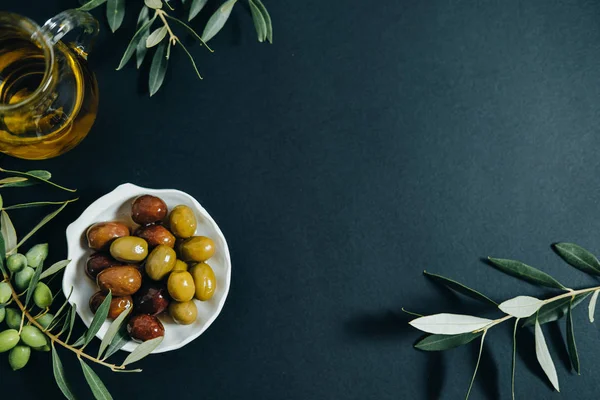 Olives, oil and green branch on black background, Top view, spac — Stock Photo, Image