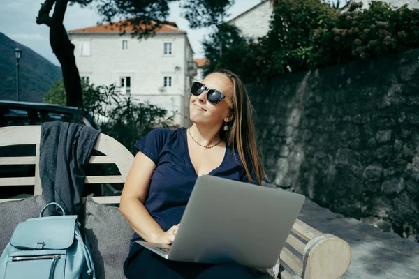 Молодая женщина фрилансер в солнцезащитных очках работает с ноутбуком в Outd — стоковое фото