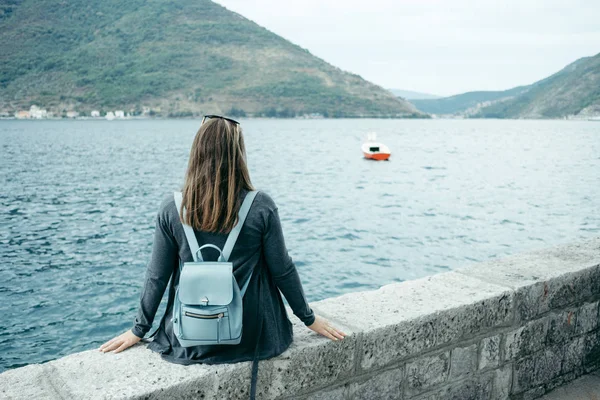 Achteraanzicht van de jonge vrouw in de grijze vest en blauwe rugzak zit — Stockfoto