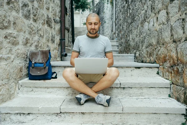 Serbest meslek sahibi adam ve sokağın ortasında bir dizüstü bilgisayar üzerinde çalışan bir gezgin.