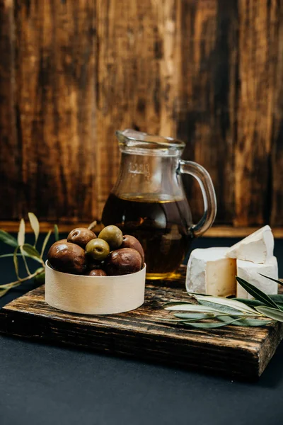 Frische dunkle und grüne Oliven, Öl, Ziegenkäse auf einem Holzbrett, — Stockfoto