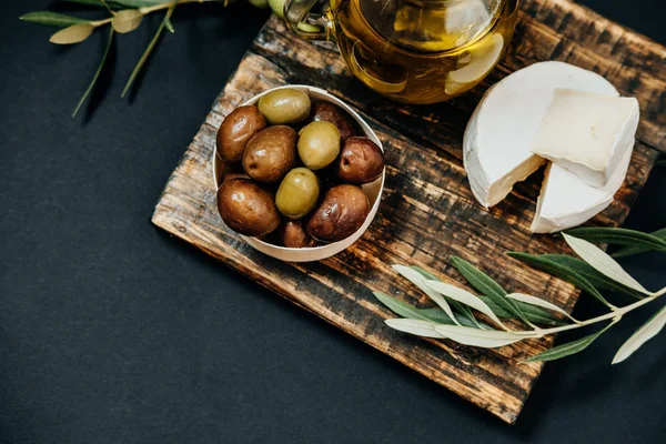 Koyu ve yeşil zeytin, petrol, keçi peyniri ahşap oyun tahtası, üst v — Stok fotoğraf