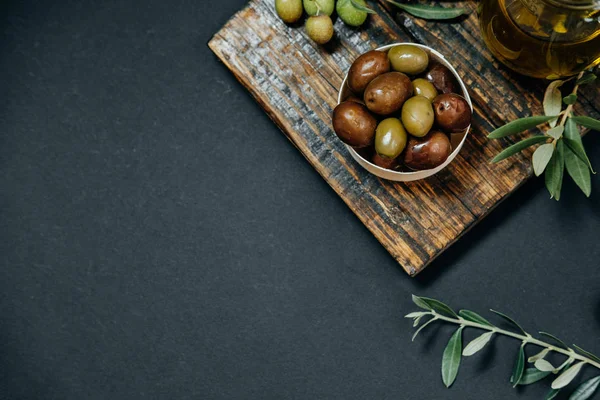 Dark and green olives, oil and leaves on a wooden board, top vie — Stock Photo, Image