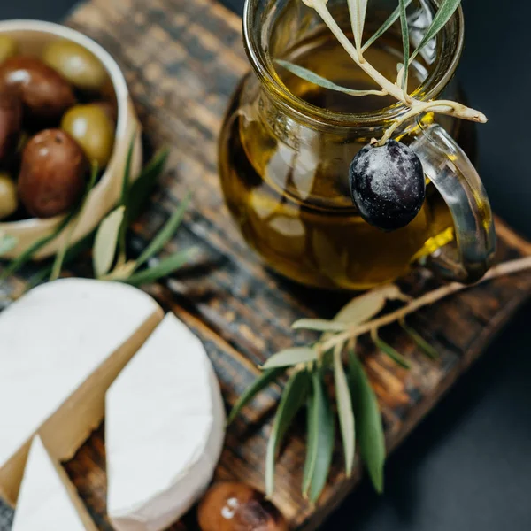 Primer plano Aceitunas oscuras y verdes, aceite, queso de cabra en un jabalí de madera — Foto de Stock