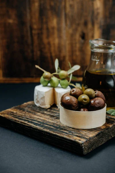 Mörk och gröna oliver, olja, getost på en träskiva — Stockfoto