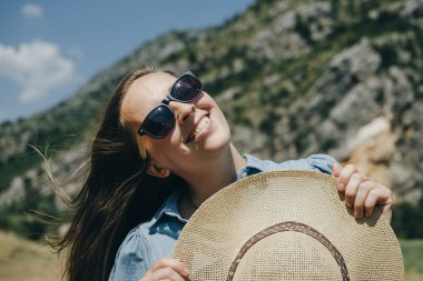 Mavi sırt çantası ve h tutan güneş gözlüğü ile mutlu kadın traveler