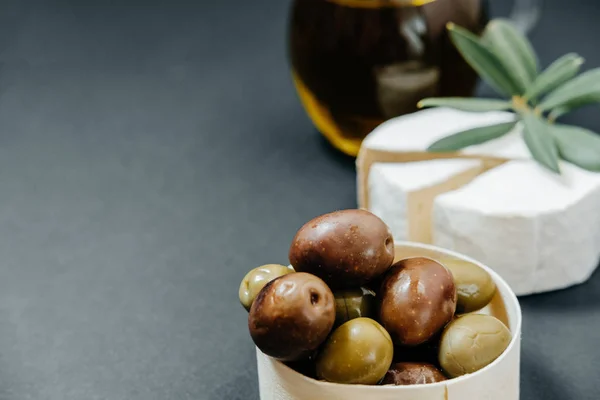 Aceitunas oscuras y verdes, aceite, queso de cabra sobre una tabla de madera —  Fotos de Stock
