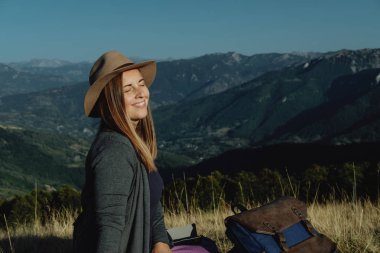 Mutlu genç kadın Gezgin m arka planda bir tepe üzerinde oturur