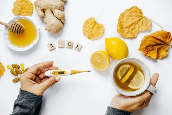Female hands with tea, Wooden word sick, lemon, thermometer, gin — Stock Photo, Image
