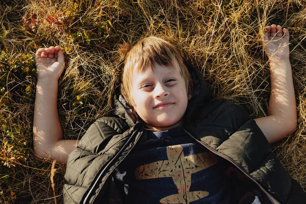Улыбающийся мальчик лежит на осенней траве в горах — стоковое фото