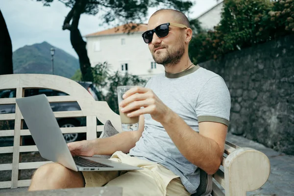 Homme aux lunettes de soleil travaille sur un ordinateur portable dans un café d'été en plein air — Photo