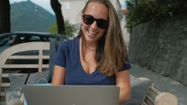 Jeune femme en lunettes de soleil communique dans les réseaux sociaux avec ordinateur portable en plein air — Video