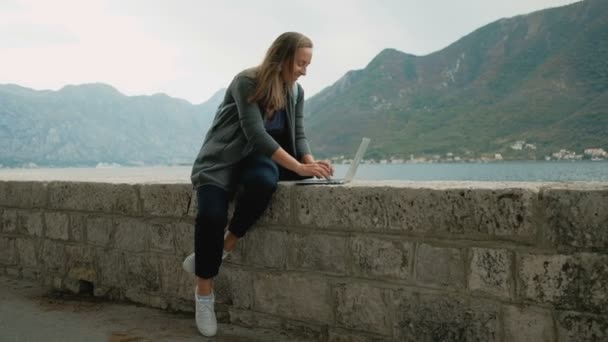 Junge freischaffende Frau in grauer Strickjacke und blauem Rucksack arbeitet am Laptop — Stockvideo