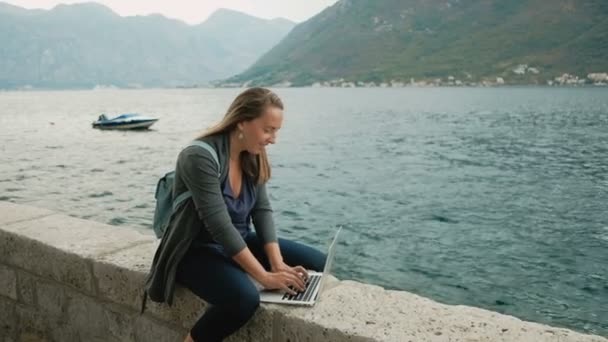 年轻的自由职业者在灰色的羊毛衫和蓝色的背包在笔记本上工作的女人 — 图库视频影像