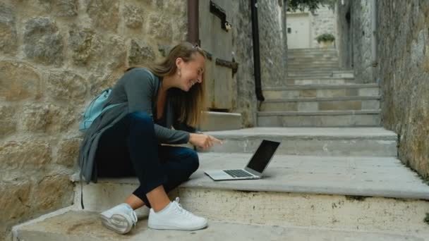 Mujer freelancer joven en cárdigan gris y mochila azul trabaja en un ordenador portátil al aire libre — Vídeo de stock