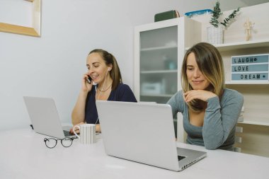 Laptop ofiste çalışan iki genç gülümseyen kadın