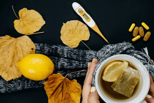 Mãos de mulher com chá, limão, termômetro, gengibre, cachecol, mesa — Fotografia de Stock