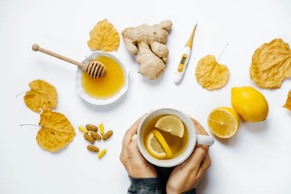 Manos de mujer con té, limón, termómetro, jengibre, miel, tabletas — Foto de Stock