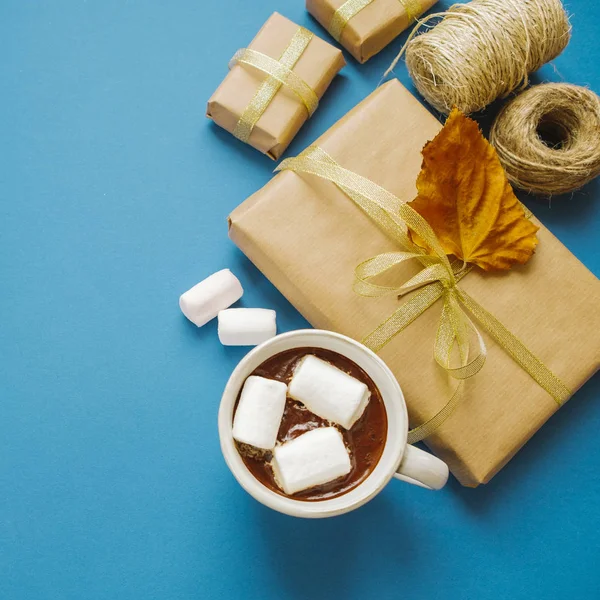Chocolate quente com marshmallows e um presente em um fundo azul , — Fotografia de Stock